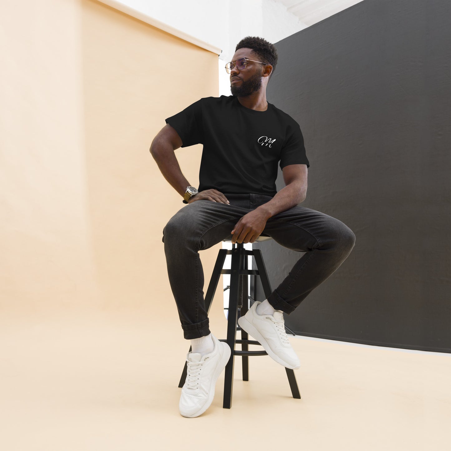 Camiseta MILLE Esencia Clásica de color negro con logo MILLE blanco en el pecho. Vista frontal de modelo sentado en un taburete.
