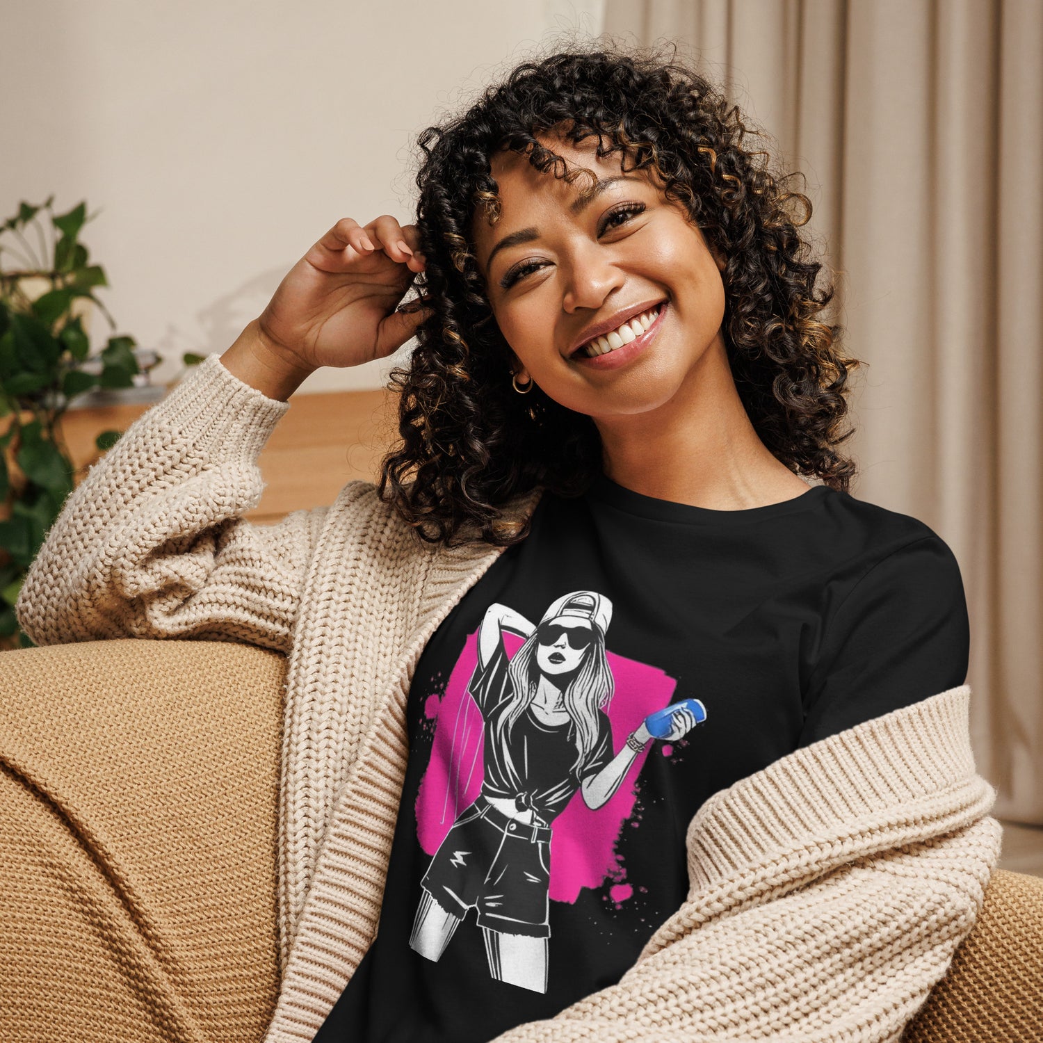Camiseta MILLE Ink Riot de color negro con diseño de chica urbana sobre mancha de tinta fucsia. Vista frontal con modelo sonriendo en un sofá.