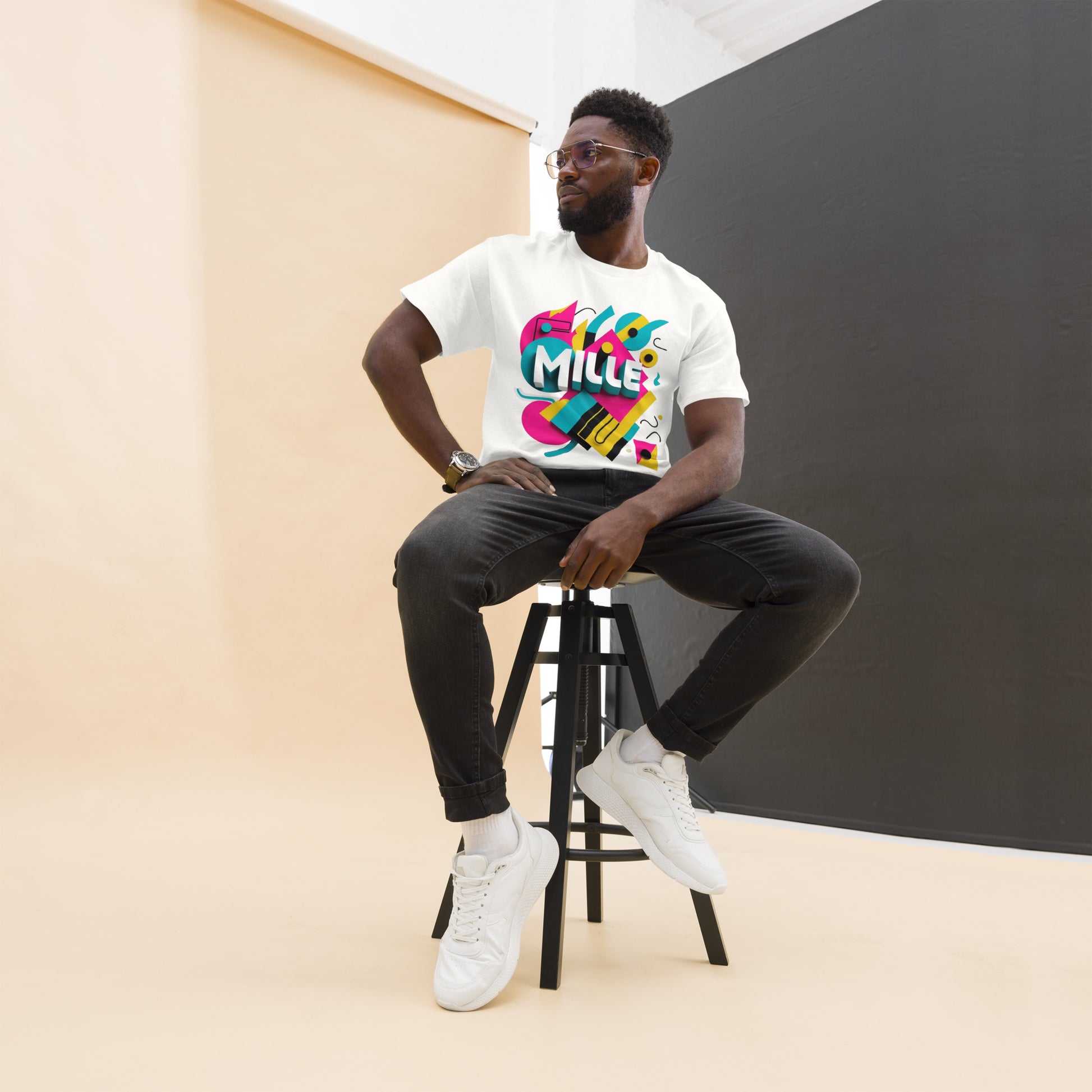 Camiseta MILLE ARCADE Tee de color blanco con diseño gráfico vibrante. Vista frontal de modelo sentado en taburete.