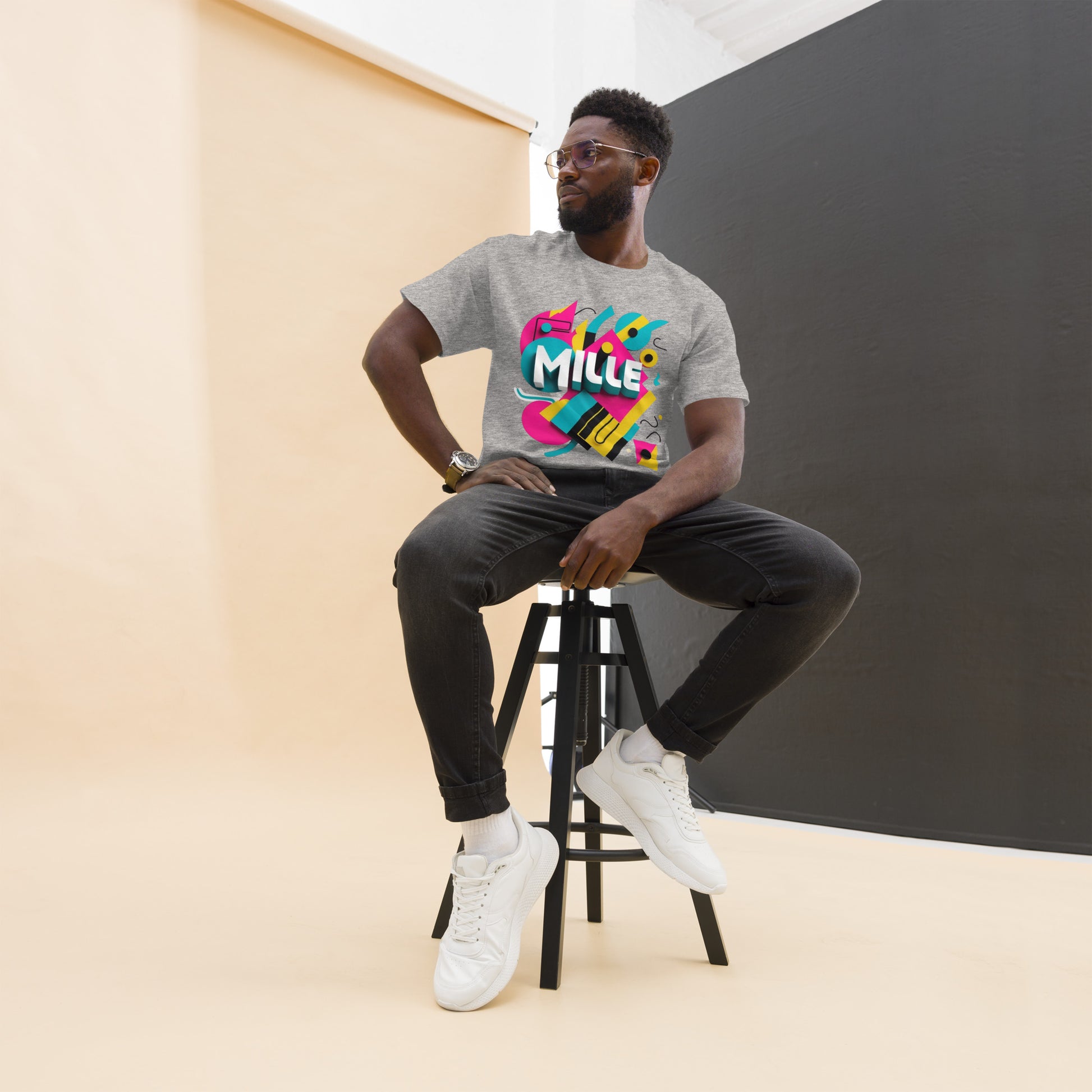 Camiseta MILLE ARCADE Tee de color gris sport con diseño gráfico vibrante. Vista frontal de modelo sentado en taburete.