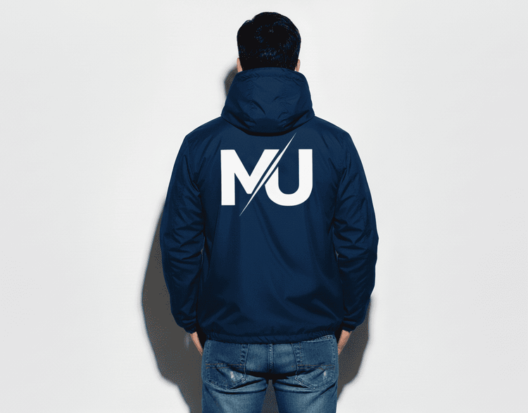 Chaqueta MILLE TEAM JACKET de color azul marino con logo grande en la espalda. Vista de espaldas de un modelo con la capucha puesta.
