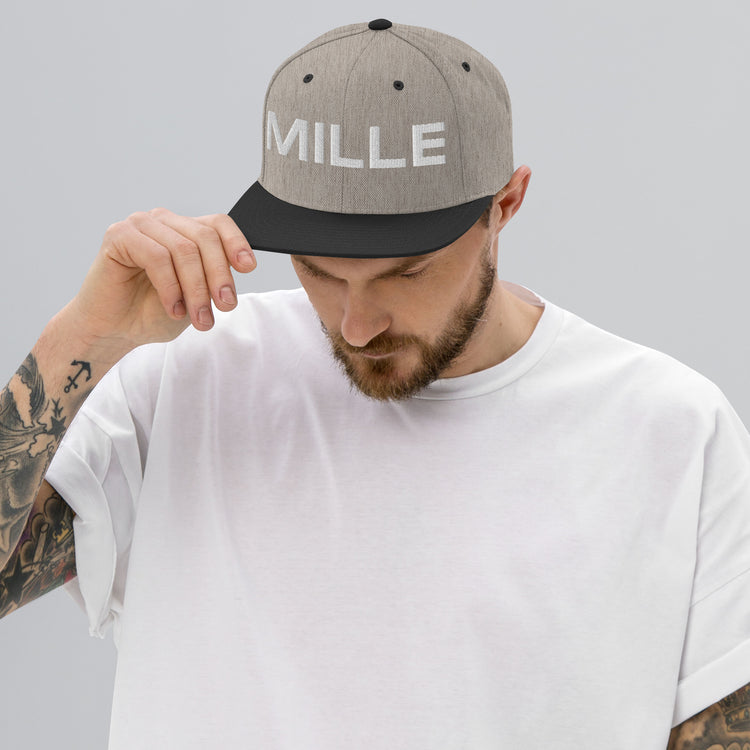 Gorra Snapback MILLE INSIGNIA de color gris jaspeado con visera negra y logo MILLE bordado en blanco. Vista frontal con modelo.