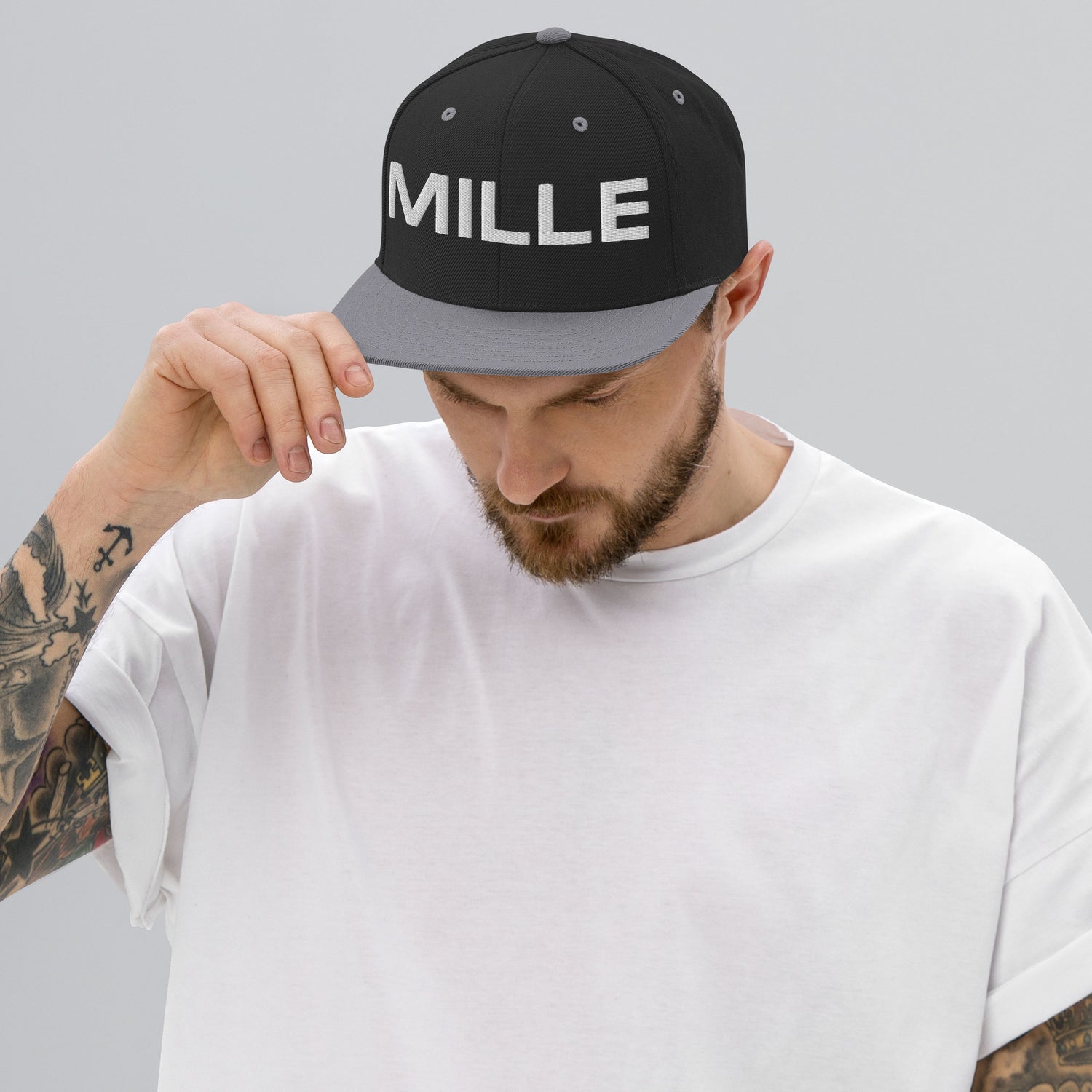 Gorra Snapback MILLE INSIGNIA de color negro con visera plateada y logo MILLE bordado en blanco. Vista frontal con modelo.