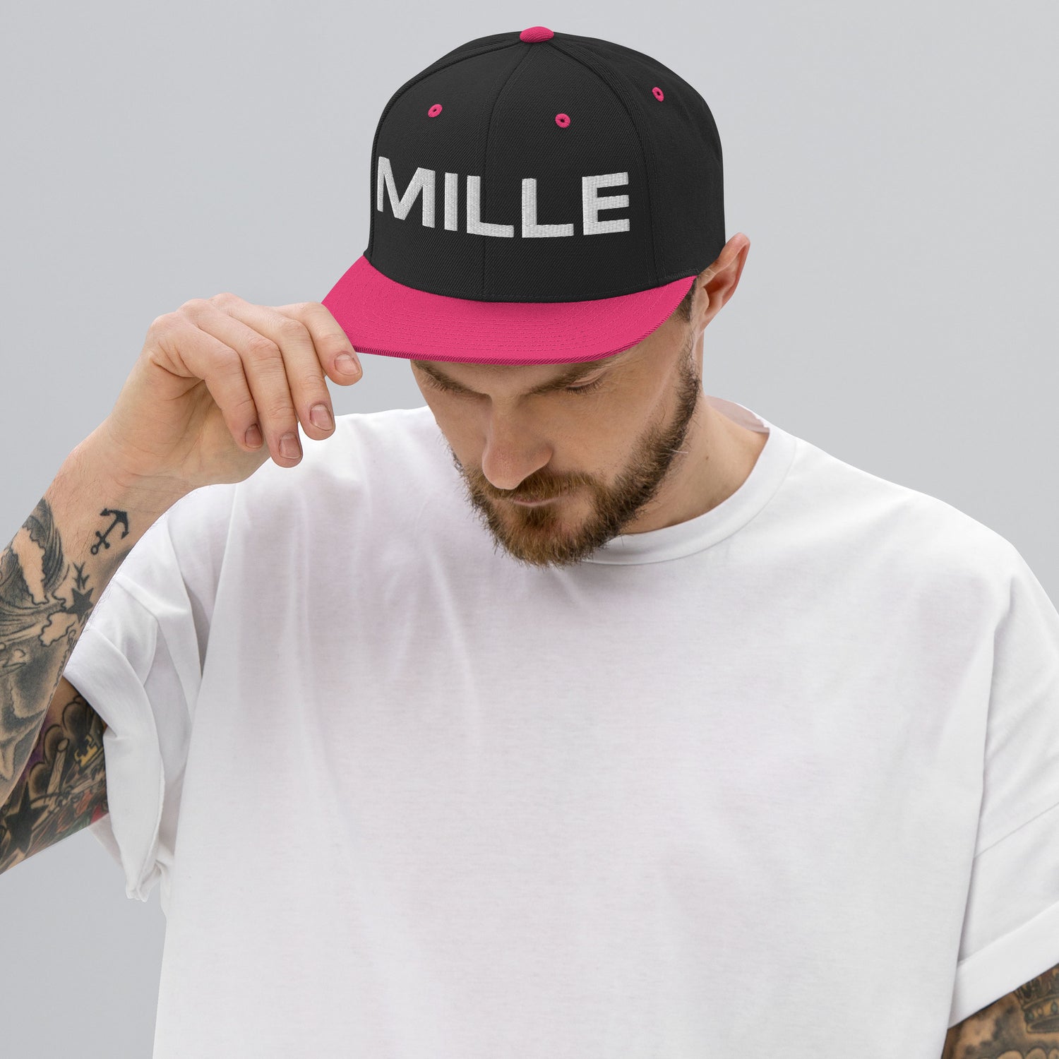 Gorra Snapback MILLE INSIGNIA de color negro con visera rosa neón y logo MILLE bordado en blanco. Vista frontal con modelo.