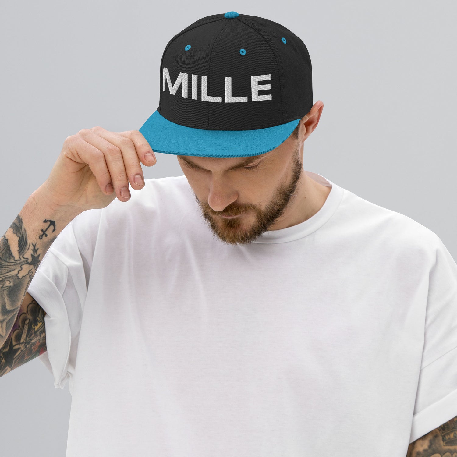 Gorra Snapback MILLE INSIGNIA de color negro con visera verde azulado y logo MILLE bordado en blanco. Vista frontal con modelo.
