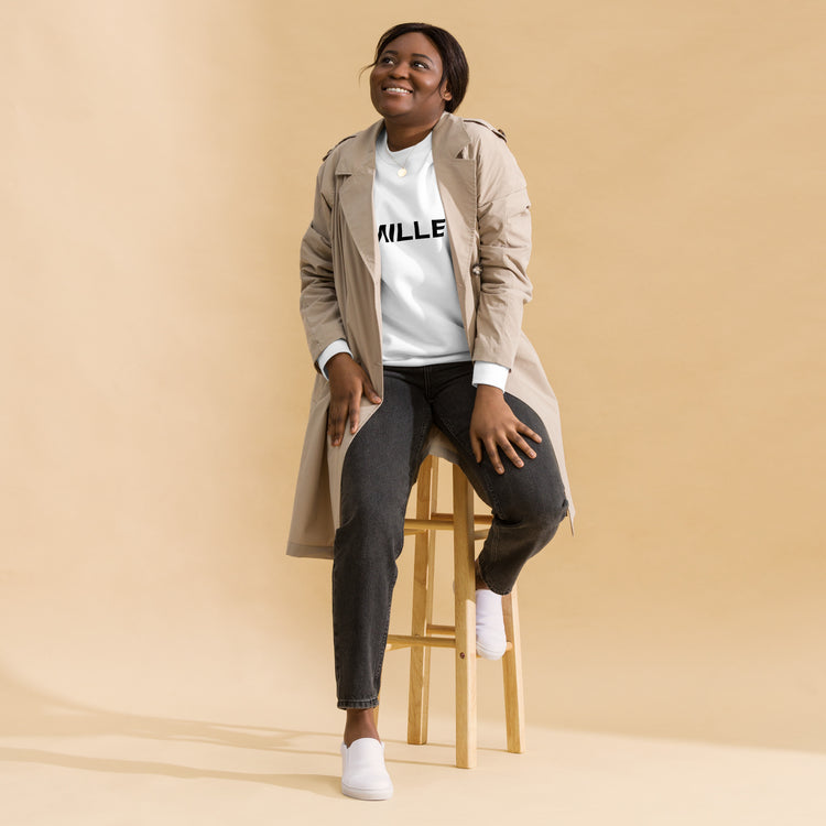 Sudadera MILLE Origin LS de color blanco con logo MILLE en el pecho. Vista de cuerpo entero con modelo sonriendo y sentada en un taburete.