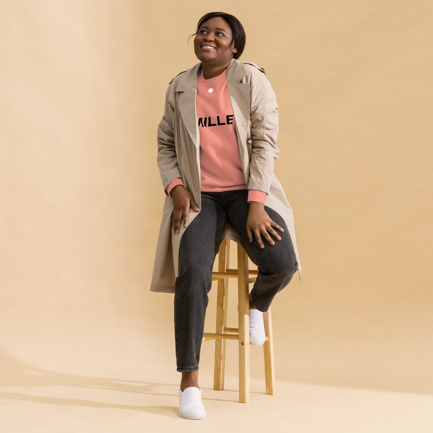 Sudadera MILLE Origin LS de color rosa empolvado con logo MILLE en el pecho. Vista de cuerpo entero con modelo sonriendo y sentada en un taburete.